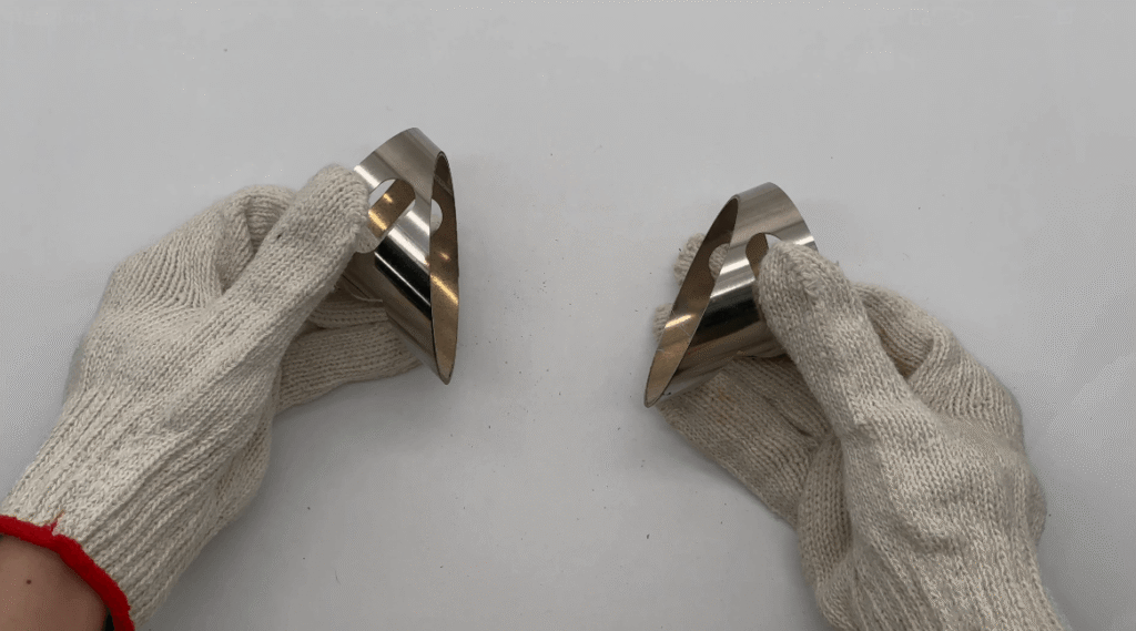 Worker wearing white gloves holding two identical laser-cut curved metal parts