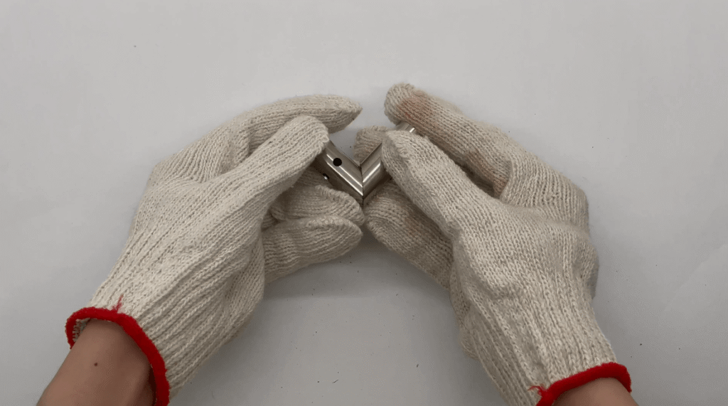 Hands in white gloves assembling a precision laser-cut angled metal tube joint