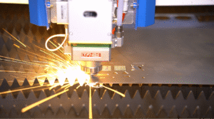 Laser cutting head working on a metal sheet, with golden sparks flying and a serrated worktable underneath