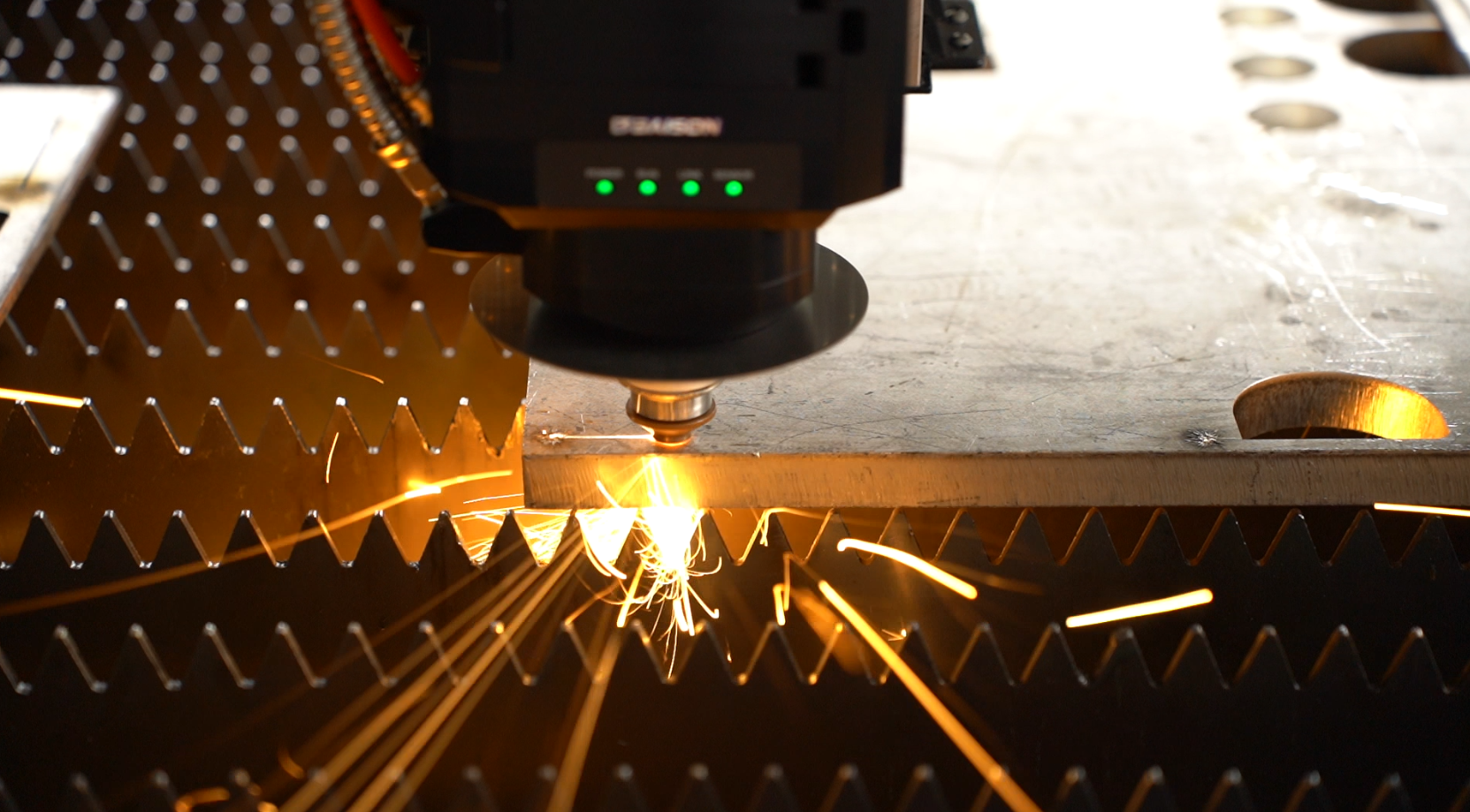 Industrial laser cutter cutting a metal sheet, with golden sparks flying and green status indicator lights on the equipment