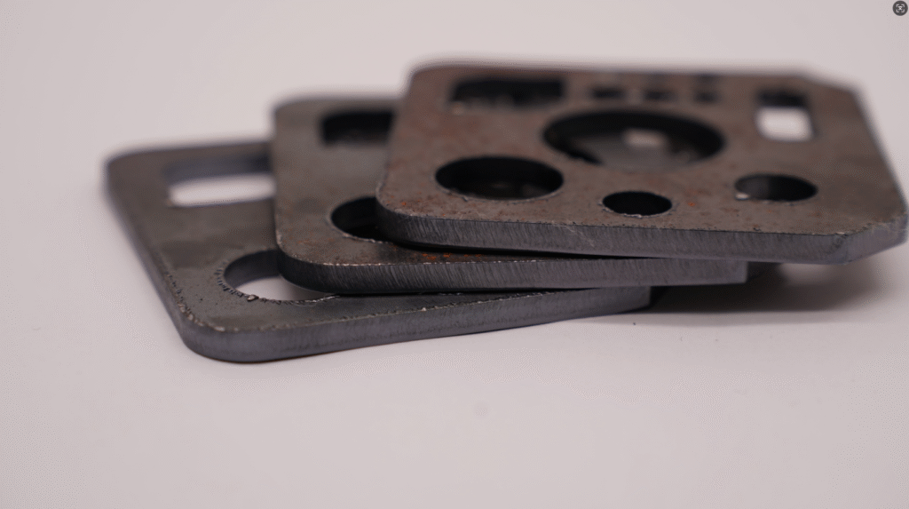 Three metal gaskets with varying degrees of burrs due to different cutting parameters, stacked on a white background