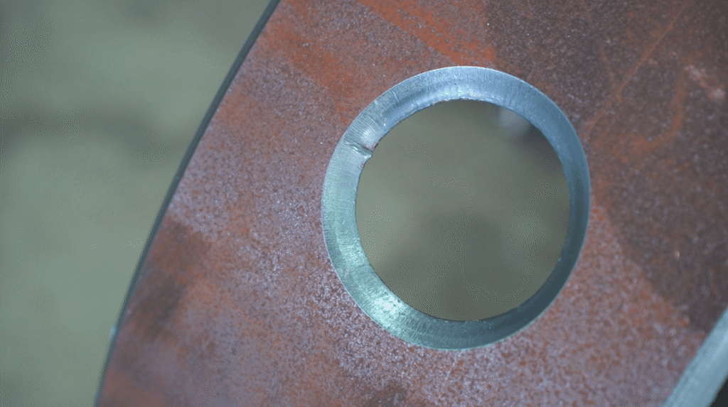 Primer plano de un orificio redondo cortado con láser en una lámina de metal.