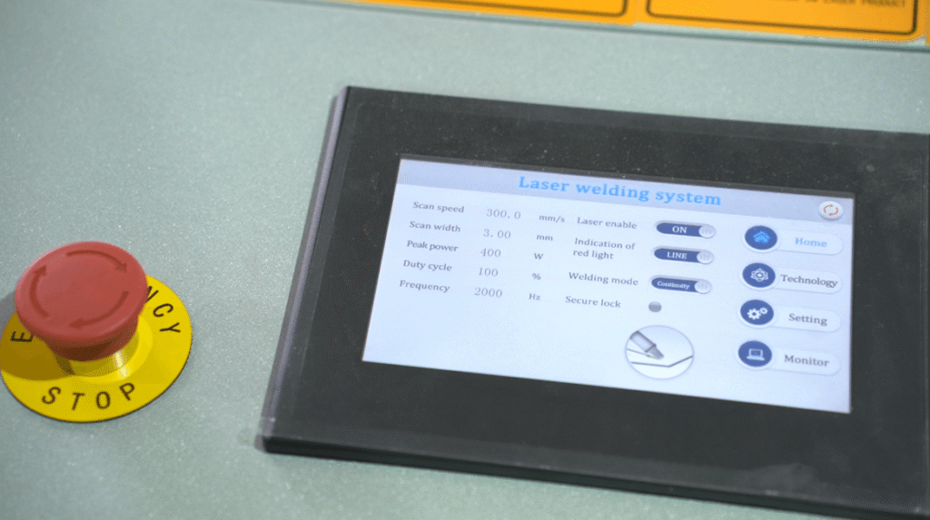 Nahaufnahme des Touchscreen-Bedienfelds einer Laserschweißanlage mit Not-Aus-Taste