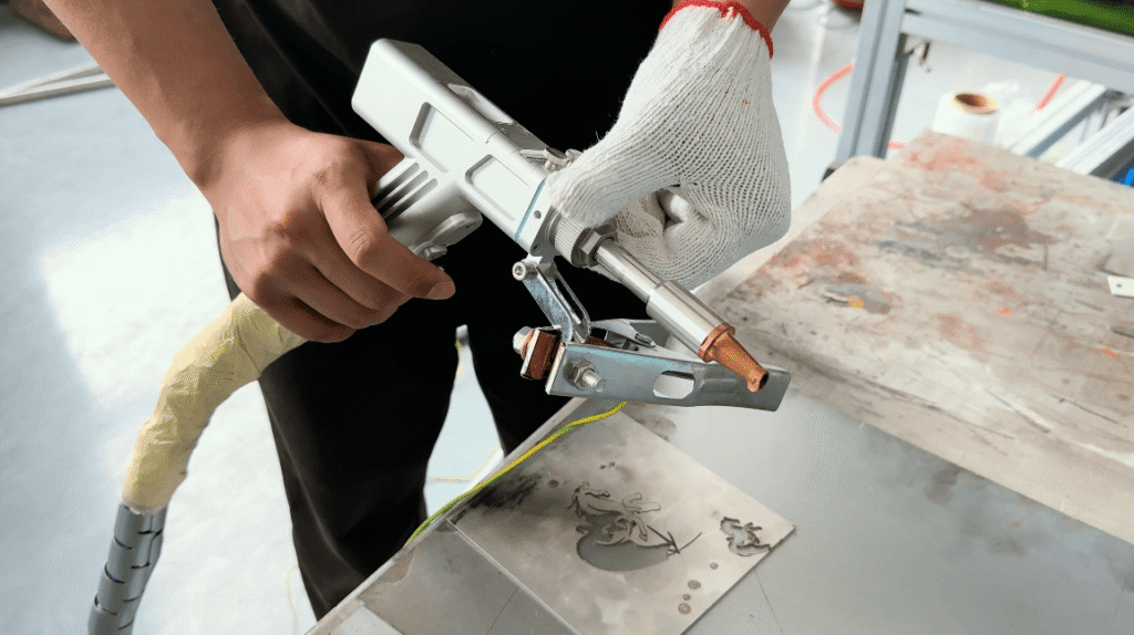 Worker holding handheld laser welding gun with copper nozzle over workbench