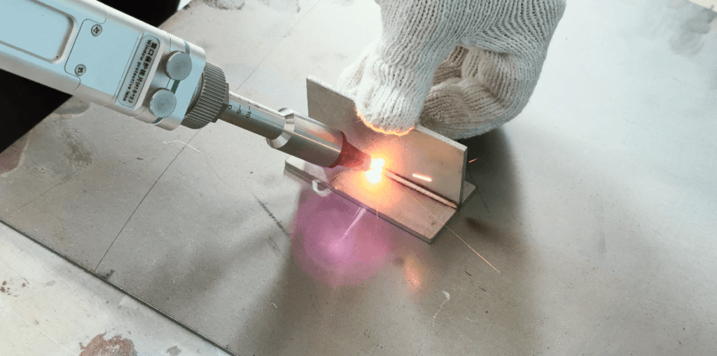 Handheld laser welding tool with wire feeder actively welding metal plate, producing purple laser glow