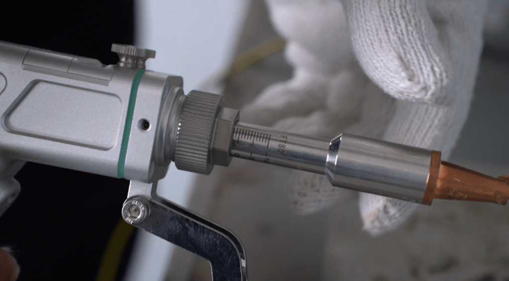 Close-up of handheld laser welding gun with FT80 scale markings and copper nozzle, held by gloved hand