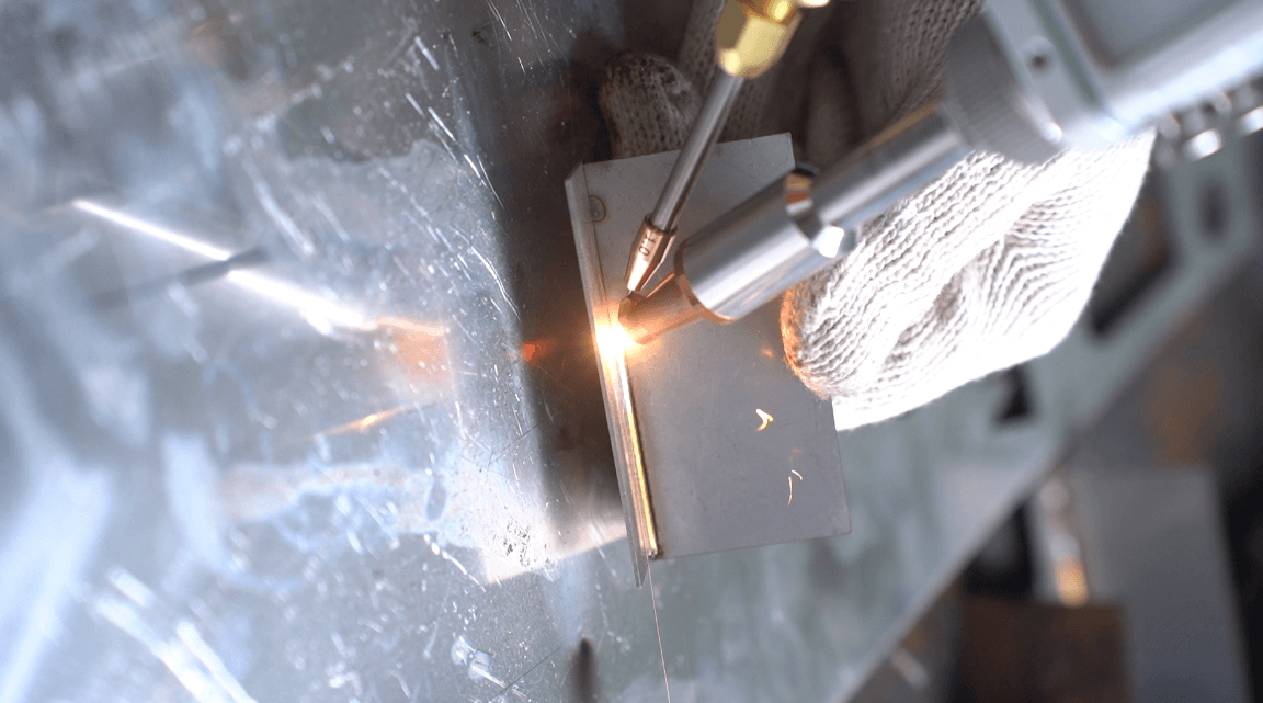 Handheld laser welding tool with wire feeder actively welding metal plate, producing bright sparks