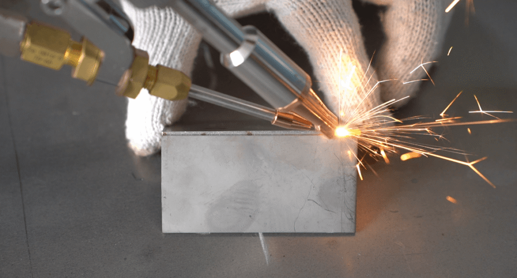 Handheld laser welder with dual nozzles creating intense sparks while joining metal plate