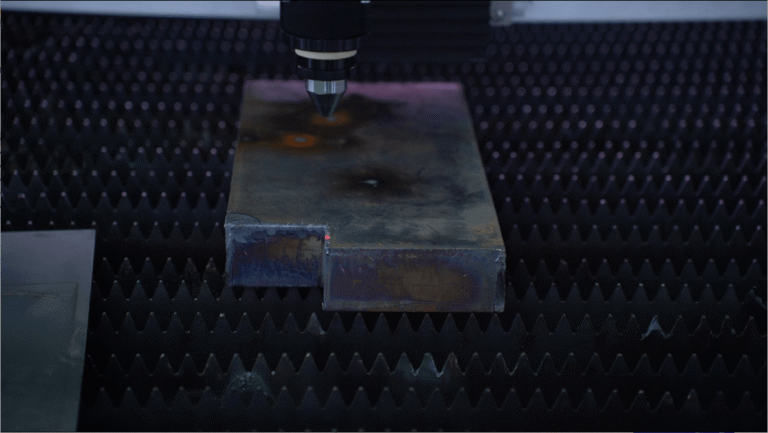 Laser nozzle aligning over a thick metal plate on a cutting bed.