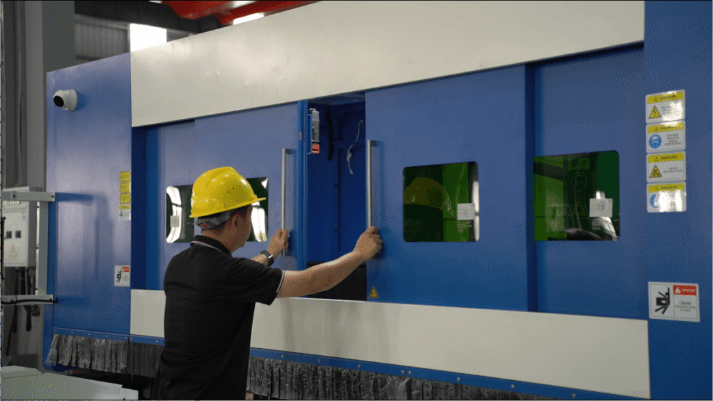 Factory engineer operating a large enclosed fiber laser cutting machine safely.