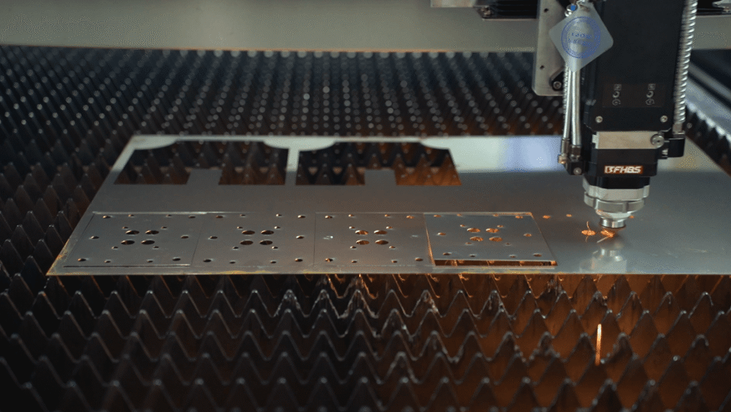Laser cutting head fabricating precision square components on a metal plate.