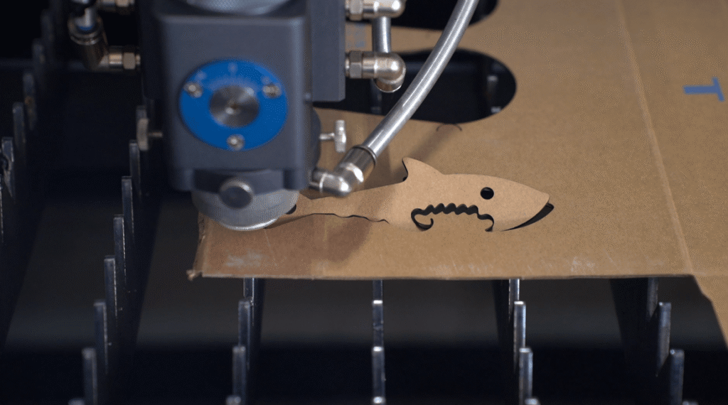 Laser cutting machine engraving a custom shark shape cardboard stencil.