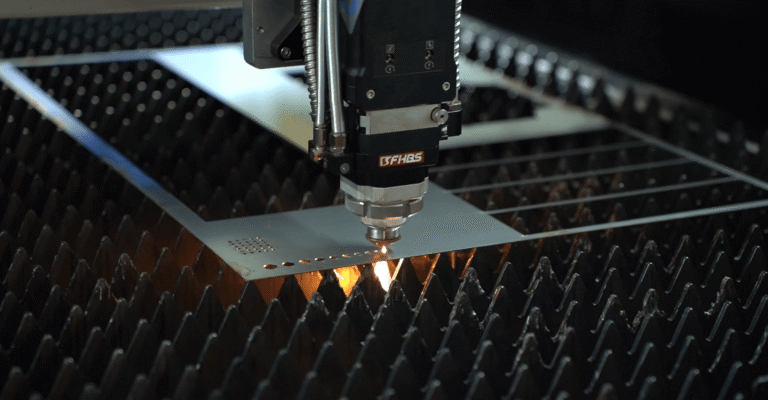 Close-up of laser head cutting metal holes with sparks.