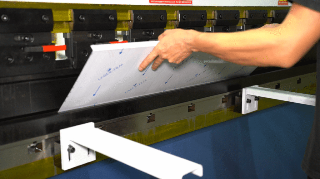 Worker positioning coated metal sheet on CNC press brake