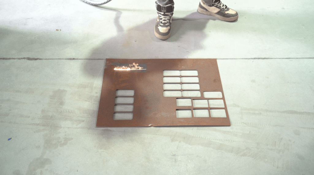 Laser beam cleaning a rusted rectangular steel grid plate.