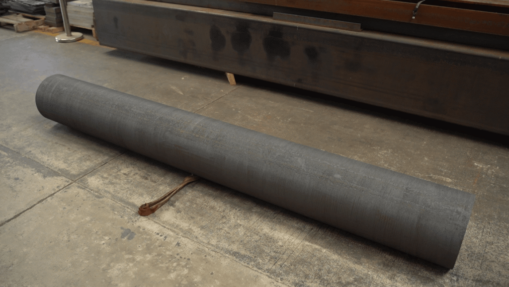 Large rusted steel pipe resting on a factory floor.